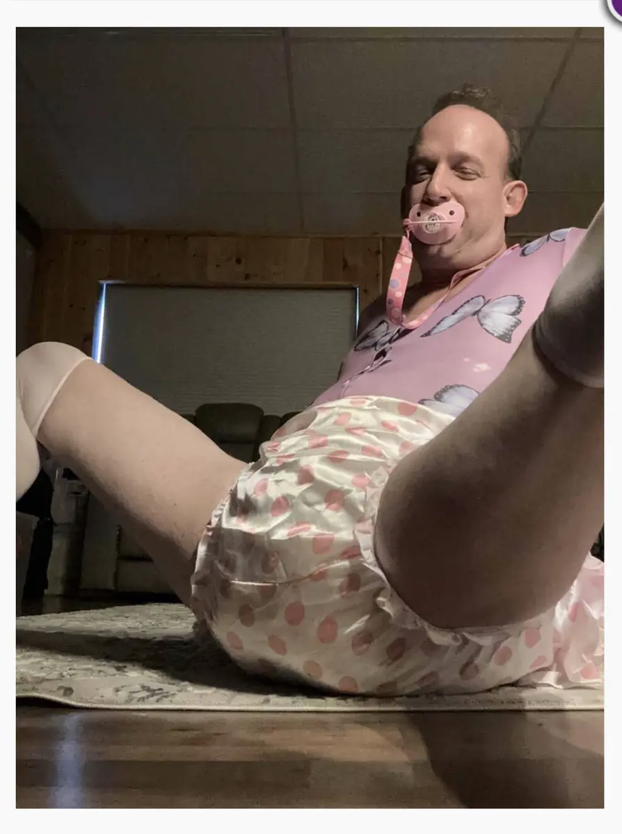 Low-angle indoor photo of a person reclining on a rug in pink clothing with a pacifier.