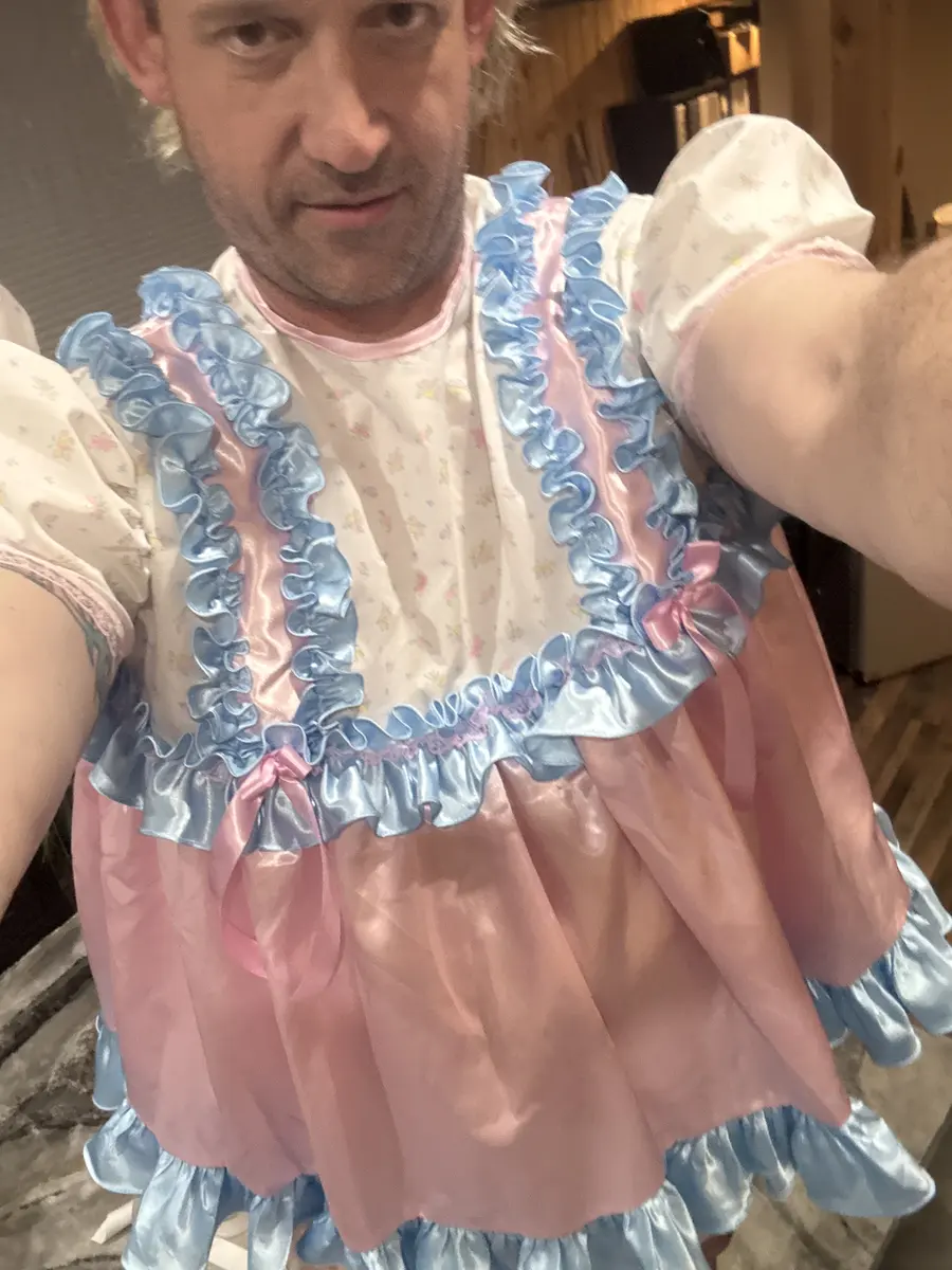 Close selfie of a man in a blue, pink, and white frilly outfit holding the camera indoors.