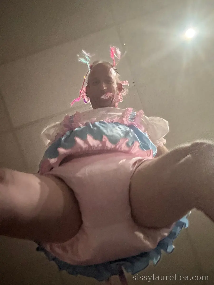 Low-angle view of a person in a pink-and-blue ruffled outfit with ribboned headpiece, shot beneath a bright ceiling light.